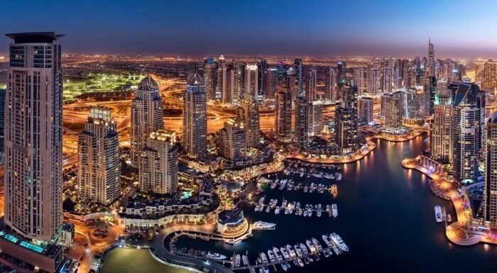 Aerial night view of Dubai Marina skyline with illuminated skyscrapers, waterfront yachts, glowing roads and city lights