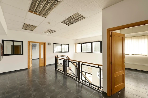 Modern commercial office interior with open corridor, tiled flooring, glass railings, wooden doors and bright natural lighting